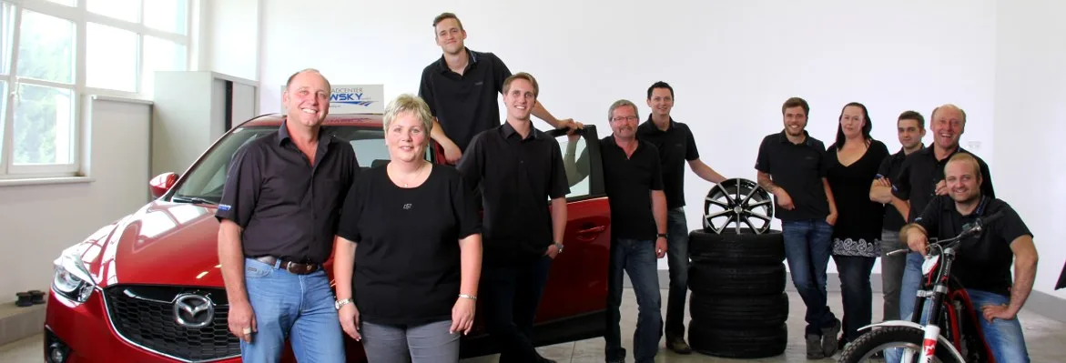 Das Team vor einem roten Mazda, daneben Reifen, Felgen und ein Fahrrad