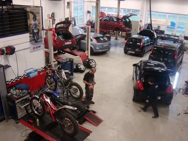 Werkstatthalle mit mehreren Hebebühnen, darauf Autos und ein Motorrad