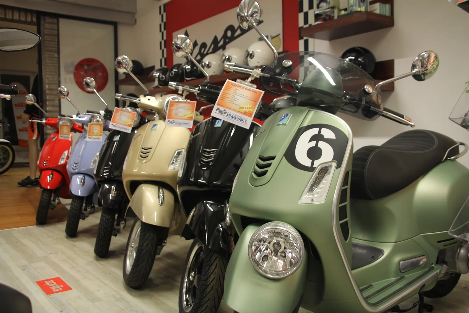 Reihe geparkter Vespa-Roller im Schauraum vor einer roten Wand