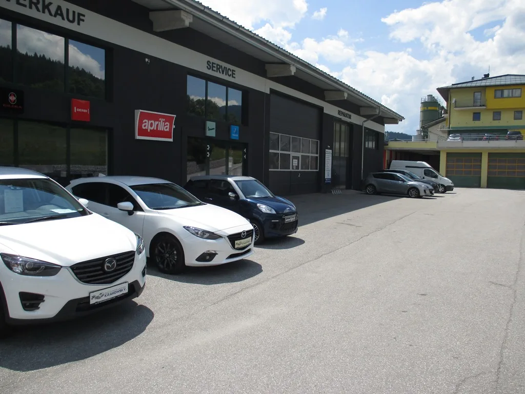 Gebäudefront mit den Beschriftungen Verkauf und Service, davor zwei weiße Mazda-Vorführwagen