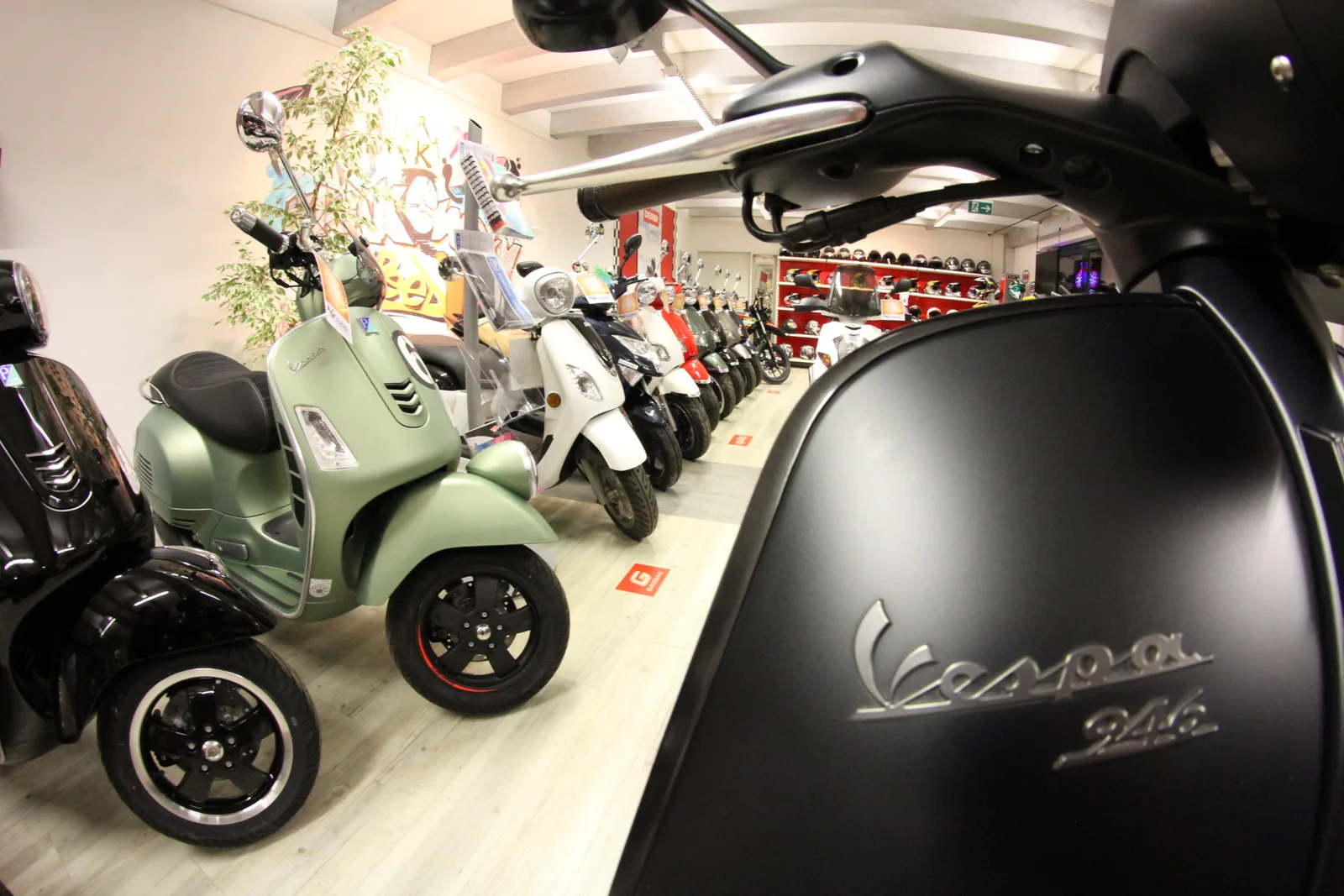 Nahaufnahme einer schwarzen Vespa 946, dahinter der Schauraum
